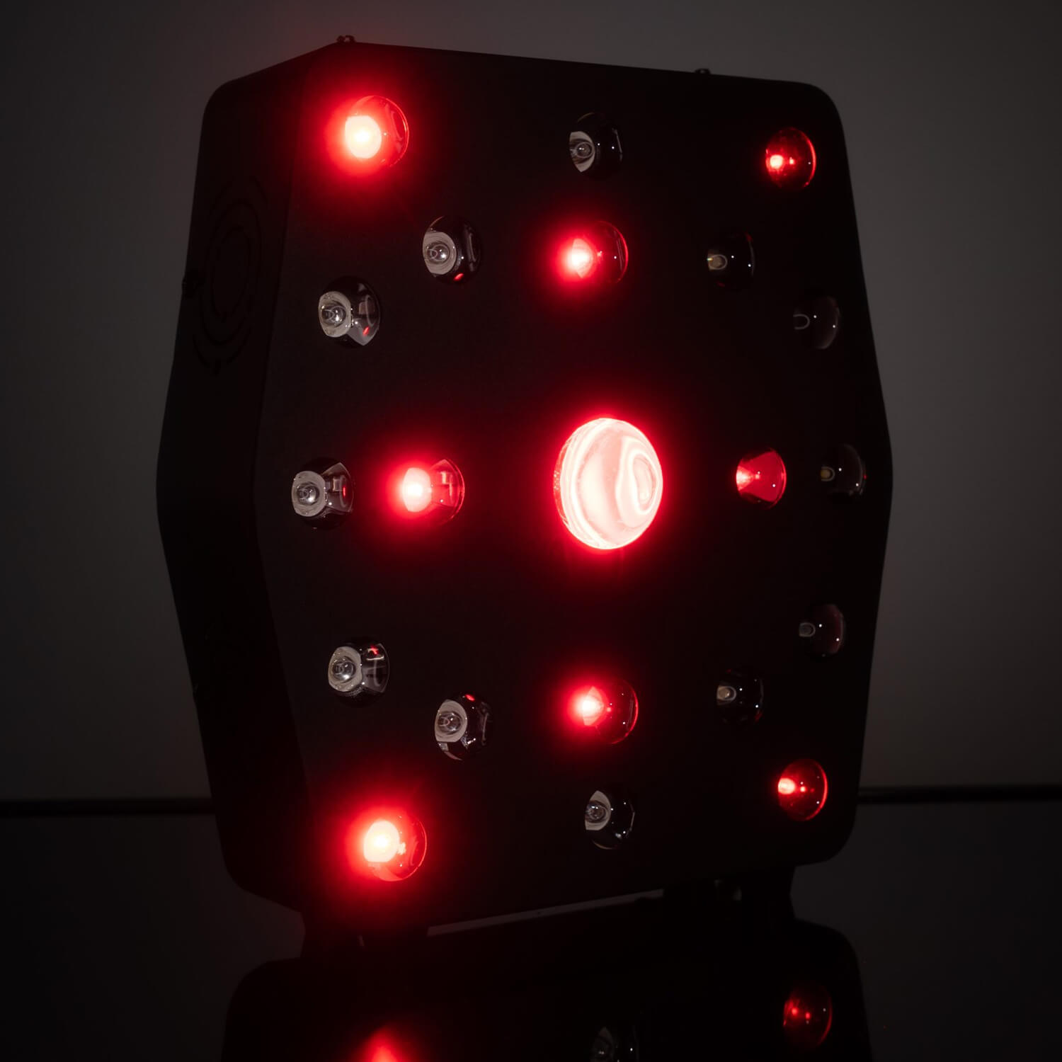 Dark rectangular LED light panel with multiple red LEDs glowing, mounted on a stand in low light.
