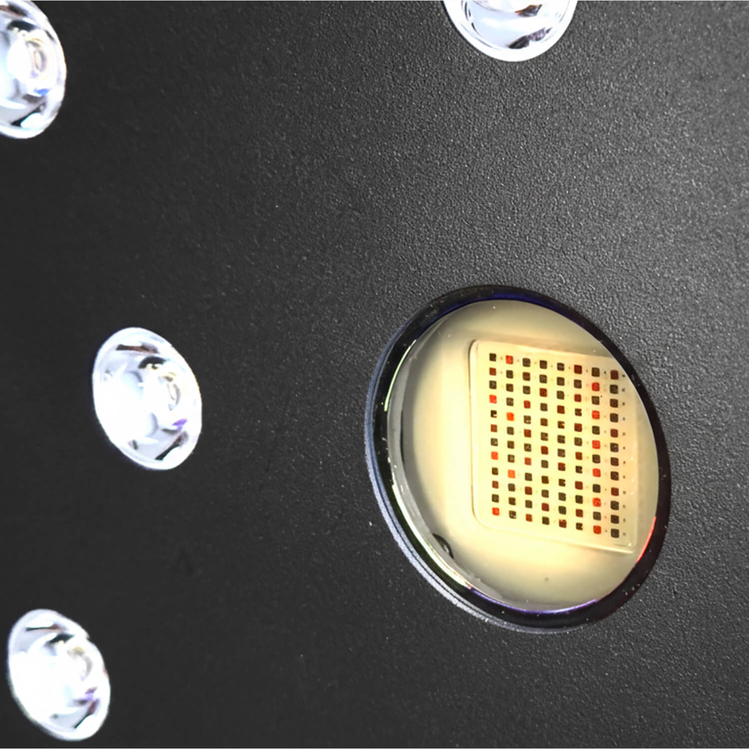 Close-up of a dark textured surface with several round metal ports; one port reveals a grid pattern inside.