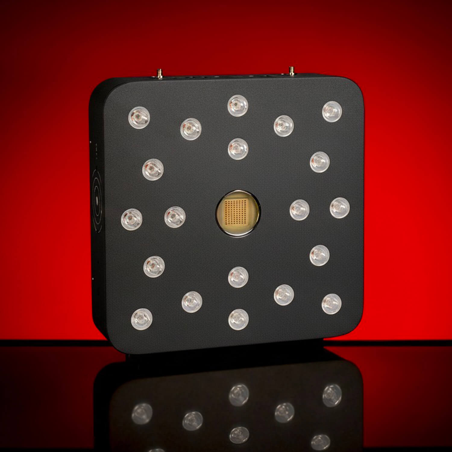 Black square electronic panel with multiple round LEDs arranged around a central chip, set against a red backdrop.