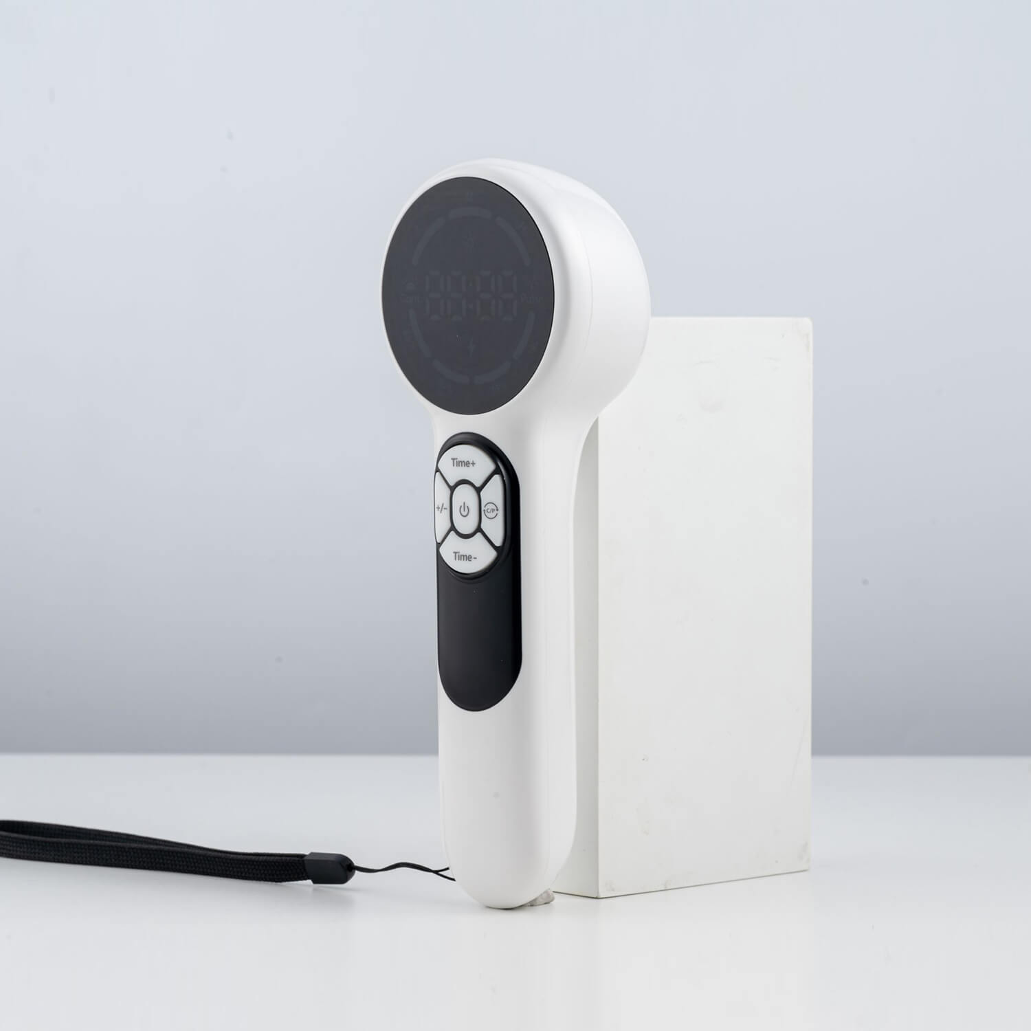White handheld massager with a circular dark head and a control panel, resting on a white block with a black strap nearby.