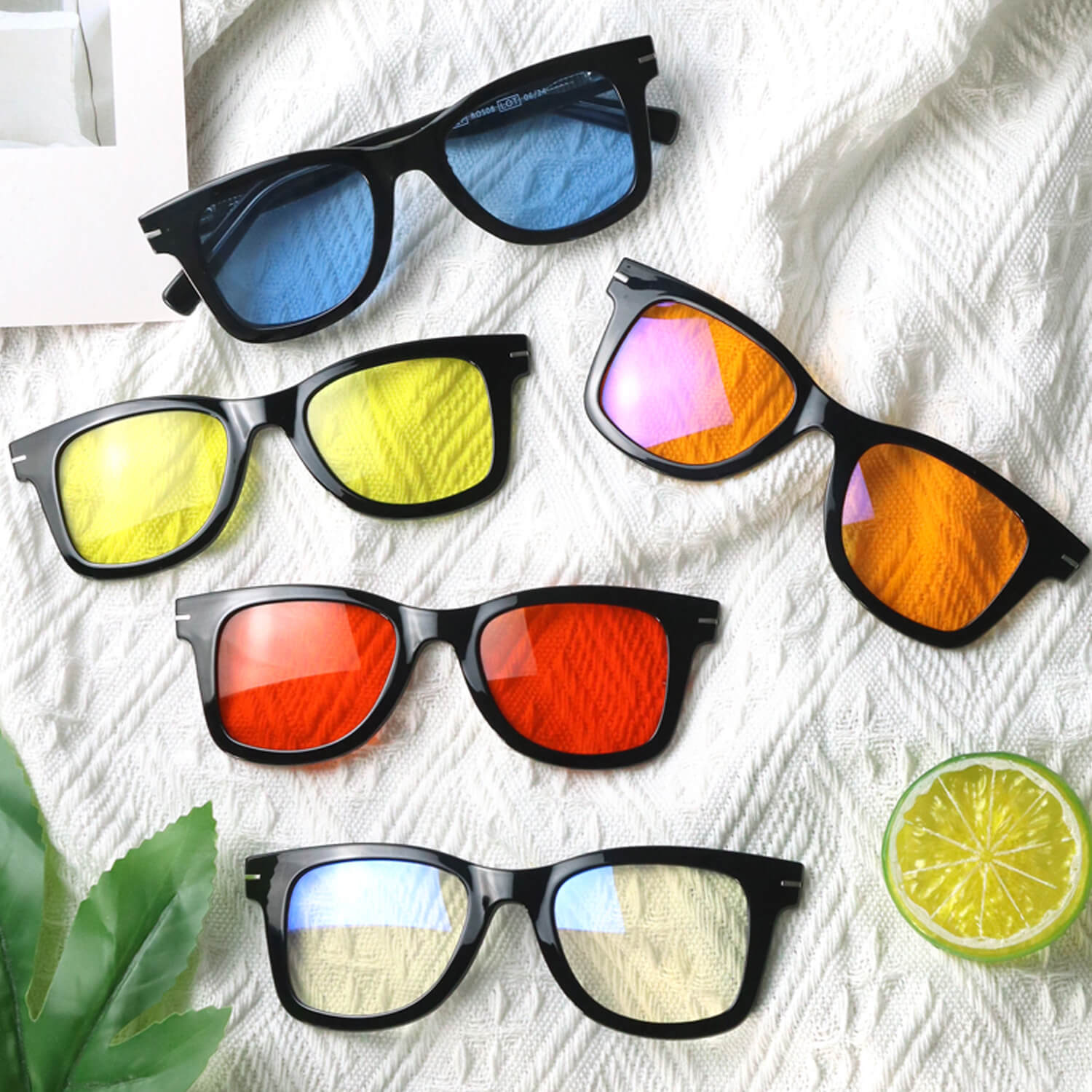 Five pairs of black-framed sunglasses with colorful mirrored lenses on a white textured blanket or cloth.