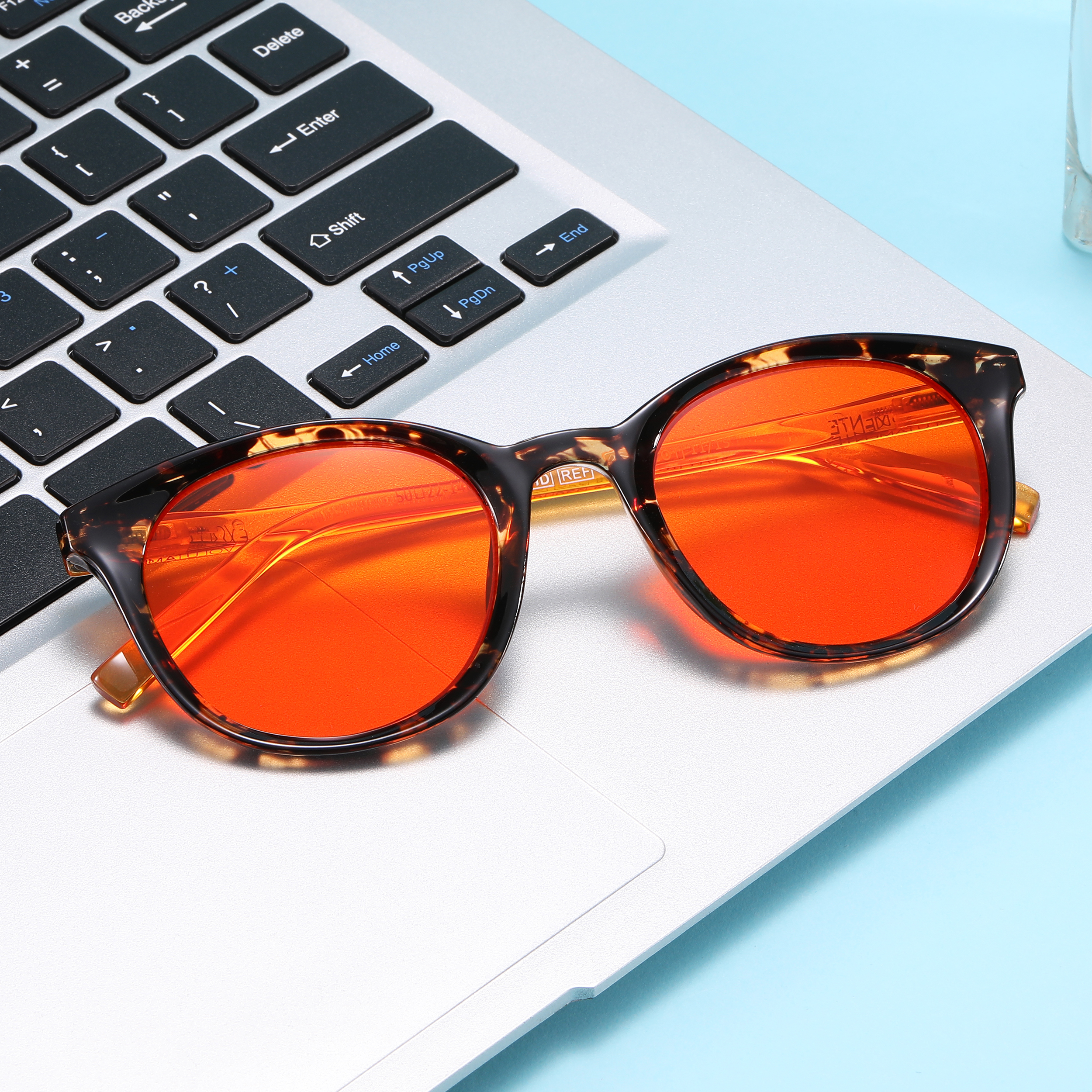 Close-up of a silver laptop keyboard with orange-tinted sunglasses resting on the palm rest area at the bottom of the frame.