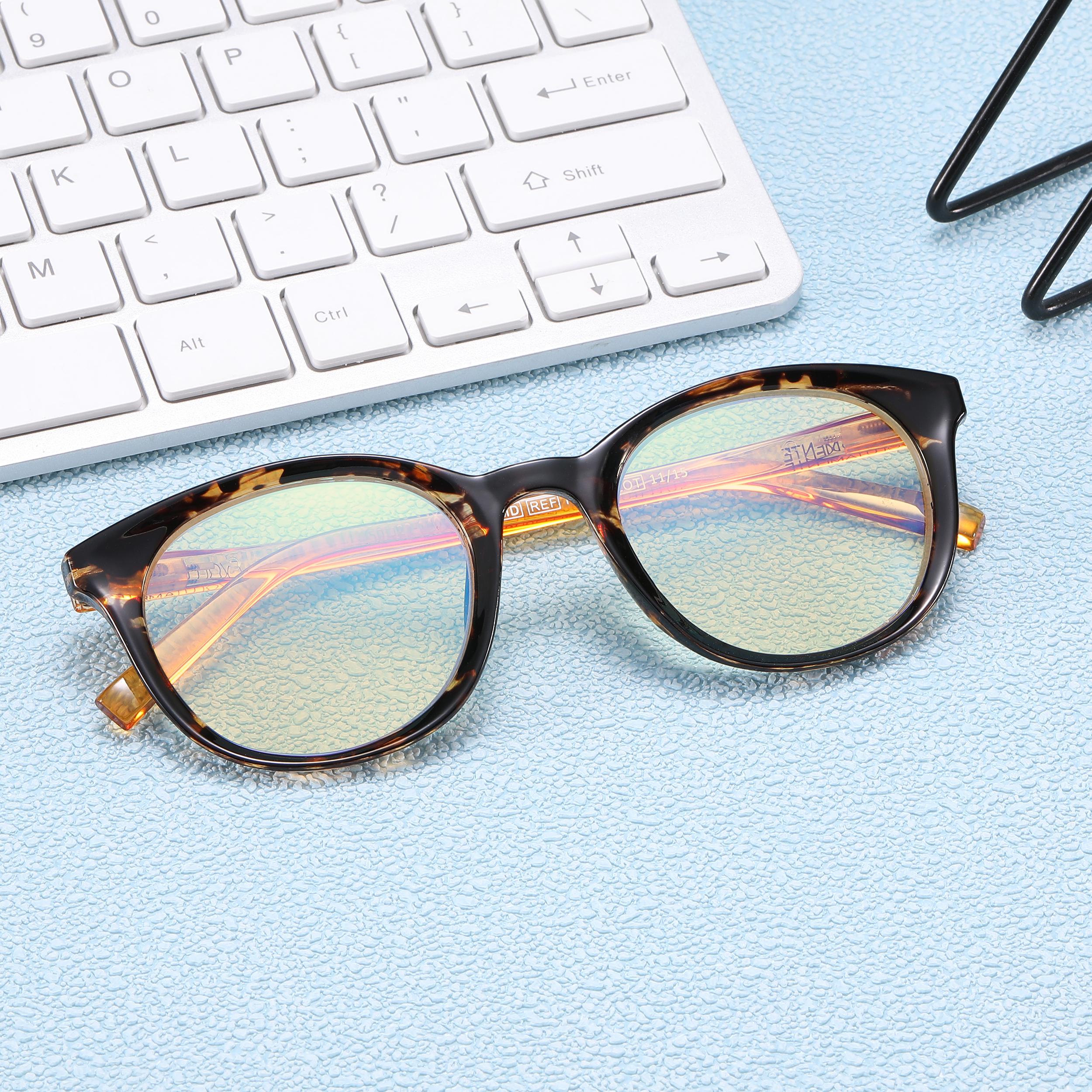 White keyboard with a tortoiseshell eyeglasses frame resting on a pale blue textured surface.